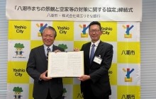 八潮市大山忍市長と株式会社埼玉りそな銀行平野隆司執行役員埼玉東地域営業本部長が協定式で協定締結を記念して協定書を掲げる様子