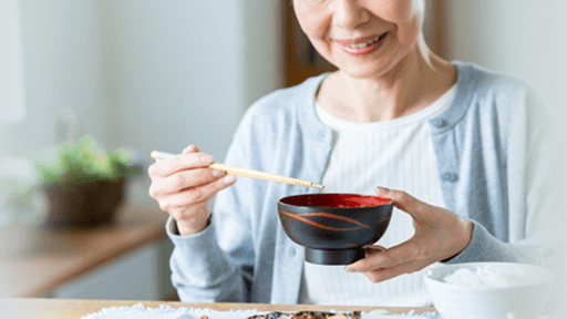 汁椀と箸を持ち、食事を摂っている女性
