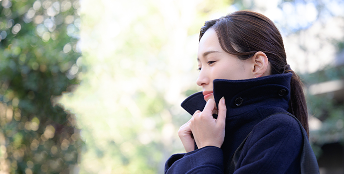 屋外でコートの襟を手で押さえる女性の横顔