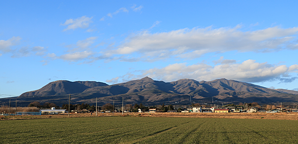 畑の向こうに山並みが見える晴天の風景写真
