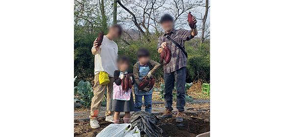 畑で大人2人と子ども2人が掘り出したサツマイモを持って立っている