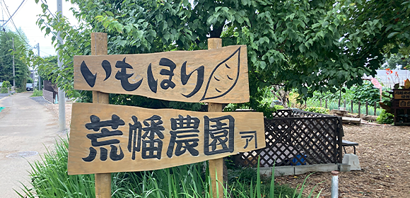 木製の看板に「いもほり」「荒幡農園」と書かれ、右向きの矢印が描かれている。
