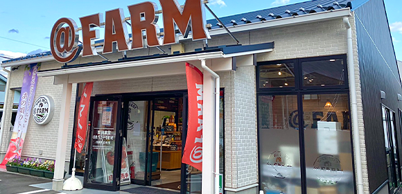「@FARM」の看板が掲げられた店舗外観。入口付近に赤いのぼりが立っている。