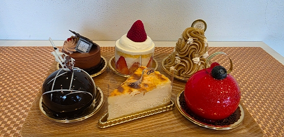 木製トレーの上に、チョコレート、いちご、モンブラン、チーズケーキ、赤いドーム型などのケーキが並んでいる。